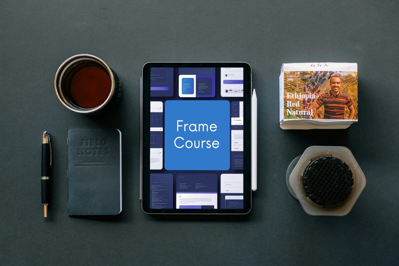 A tablet centered on a dark tabletop, displaying a blue screen with the words 'Frame Course.' Surrounding it are a notebook with 'FIELD NOTES' on the cover, a pen, a cup of tea, a small book or card, and a hexagonal container.