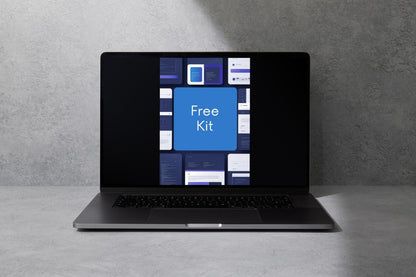 A dark gray laptop sits open on a light gray surface against a textured gray wall, with its screen displaying a blue and white interface that reads 'Free Kit'.